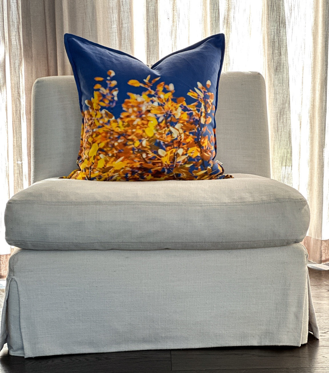 Aspen Sky pillow styled on a neutral linen chair — golden aspen leaves against a deep blue Utah sky creating a bold, modern mountain look